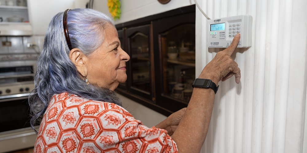 Mujer ingresando los dígitos de recarga de energía prepago en el medidor, ubicado en la pared.