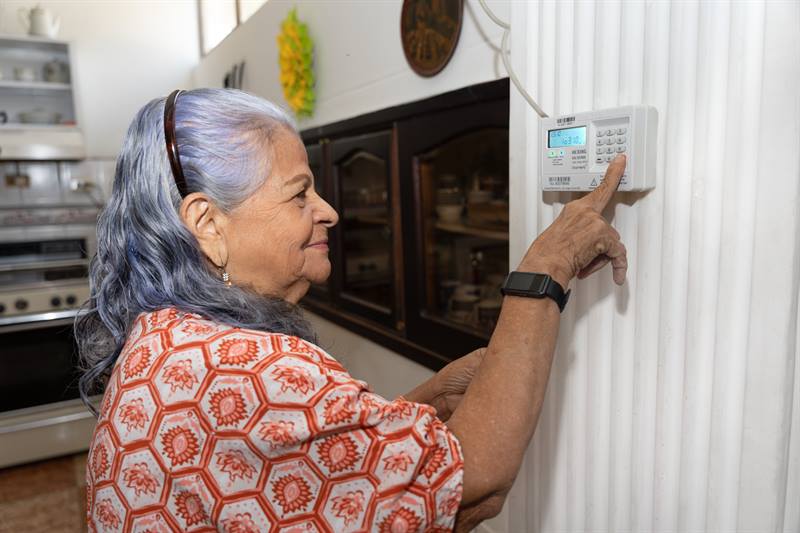 Mujer ingresando los dígitos de recarga de energía prepago en el medidor, ubicado en la pared.