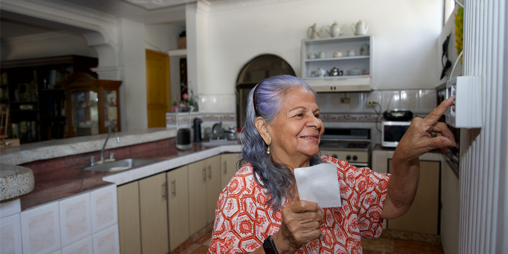En la imagen se ve una mujer haciendo el proceso de recarga de energía en el medidor prepago de su casa.
