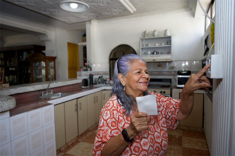 En la imagen se ve una mujer haciendo el proceso de recarga de energía en el medidor prepago de su casa.
