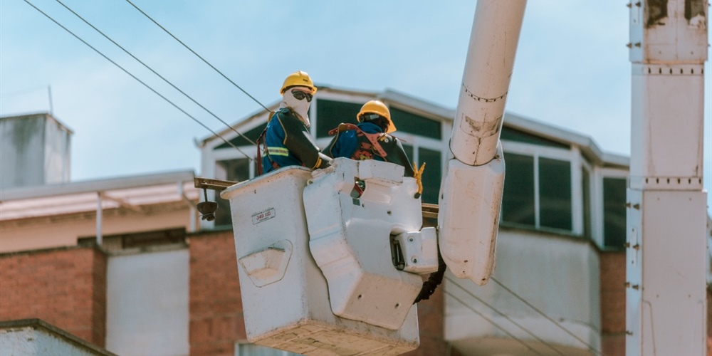 Un par de trabajadores están en un carro canasta, realizando labores sobre las redes de energía.