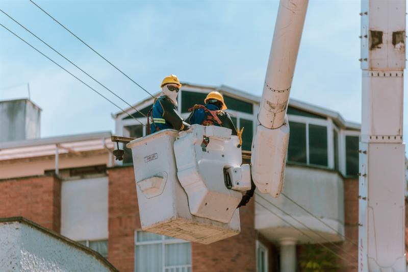 Un par de trabajadores están en un carro canasta, realizando labores sobre las redes de energía.