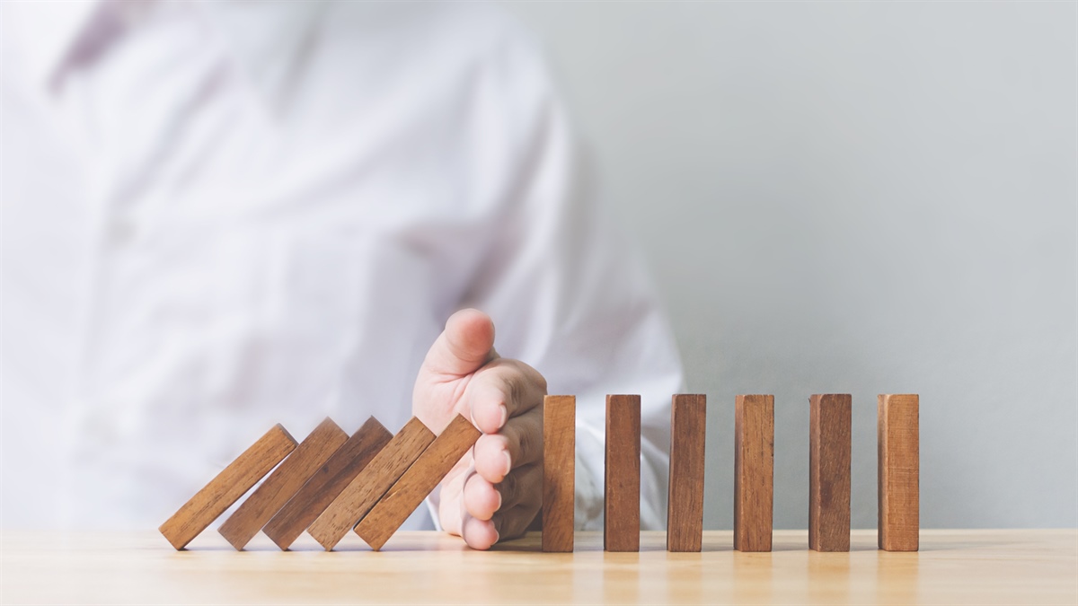Fotografía-de-fichas-de-domino-en-equilibrio-y-una-persona-interrumpiendo-la-caída